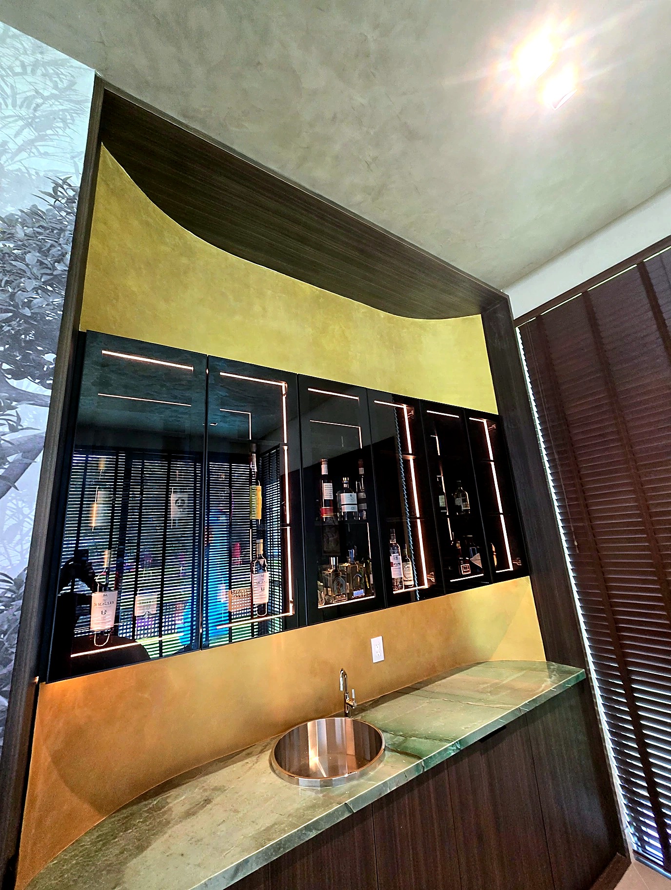 Bar area with golden metallic plaster backsplash behind backlit display cabinets