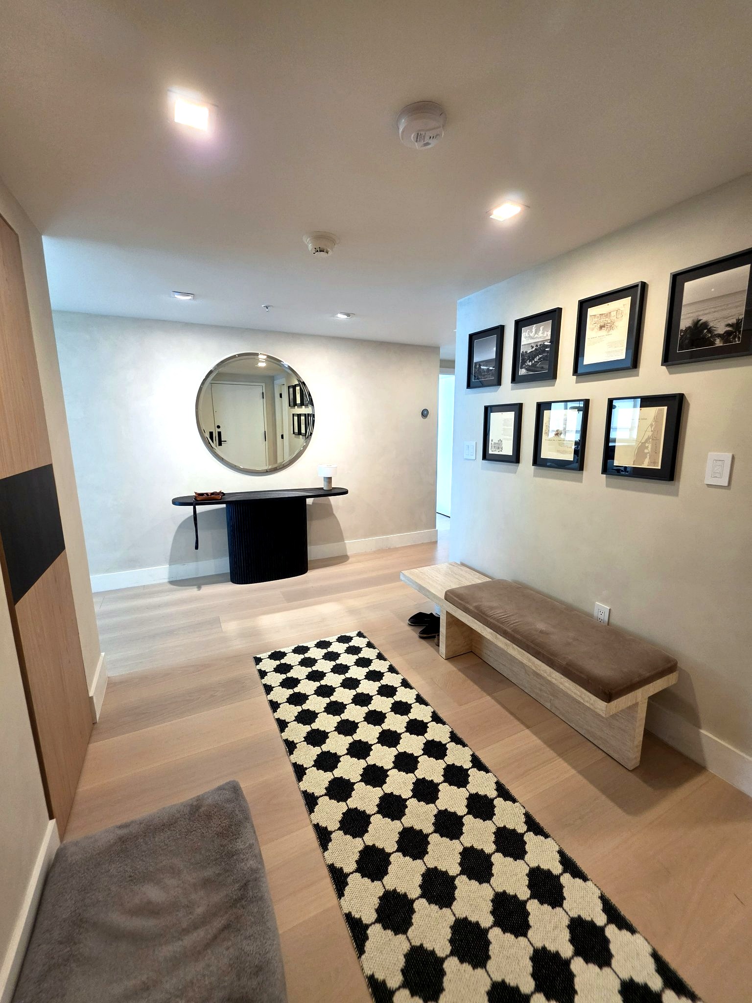 Entry gallery with a round mirror, bench and hand-applied limewash walls in a Bal Harbour residence