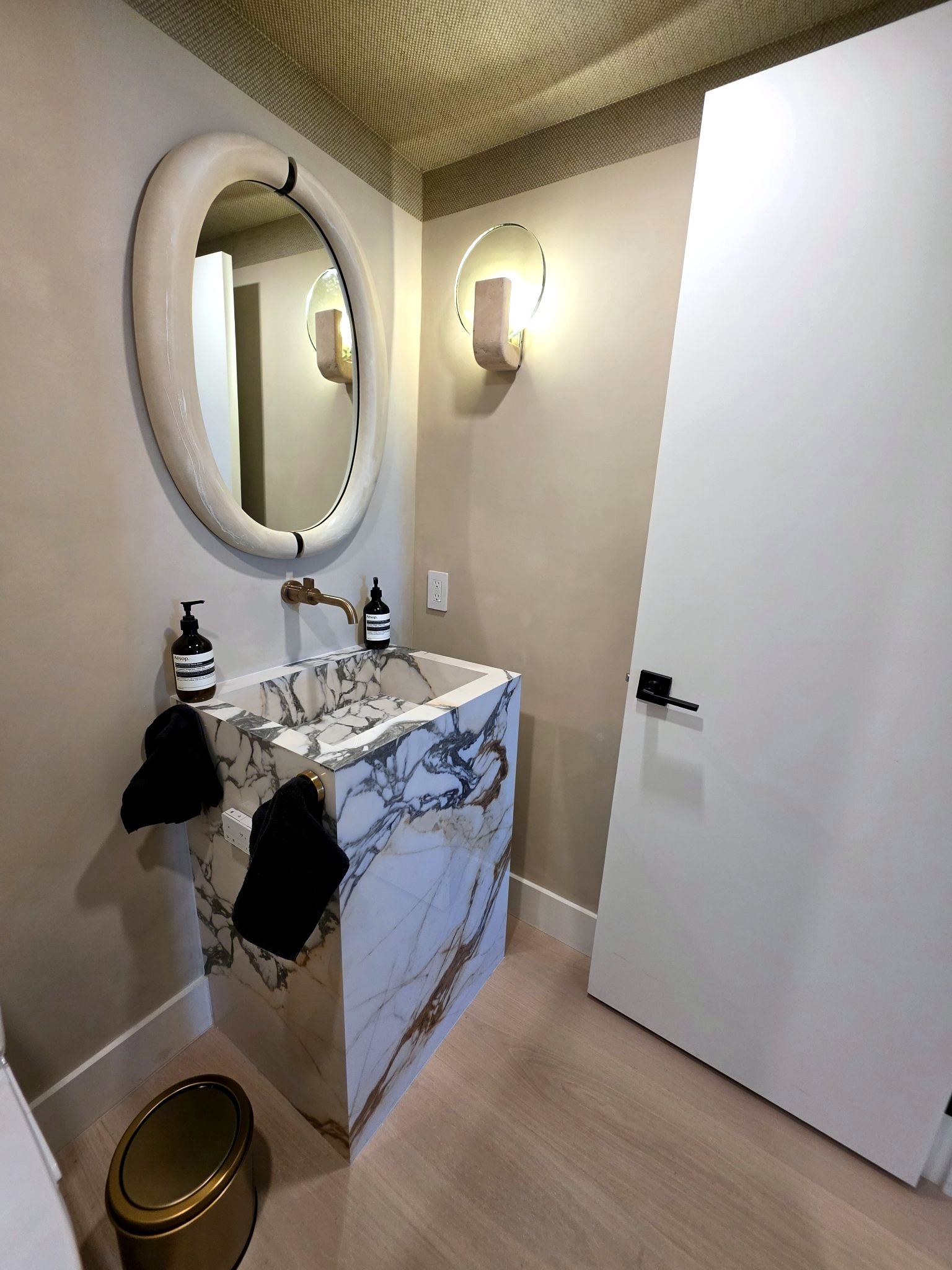 Marble powder room with an oval mirror and hand-applied limewash walls in a Bal Harbour residence